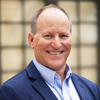 Pat O'Connor, TAG CXO Fractional Executive CIO, smiles in a suit against a backdrop of windows.